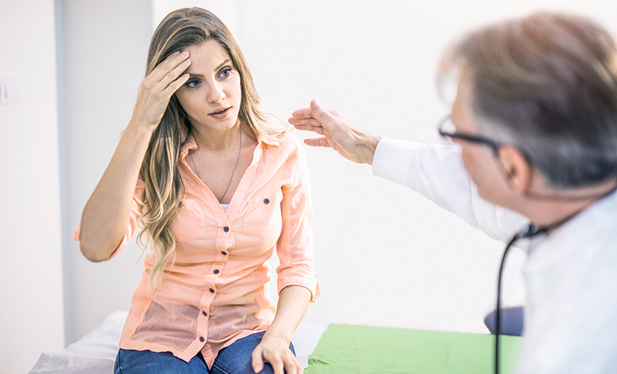 Young woman with a headache talking with her doctor.